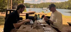 Trystan Cavitt and Robert Furberg sit at a bench overlooking Mystery Lake Scuba Park as they prepare a Holter Monitor for deployment