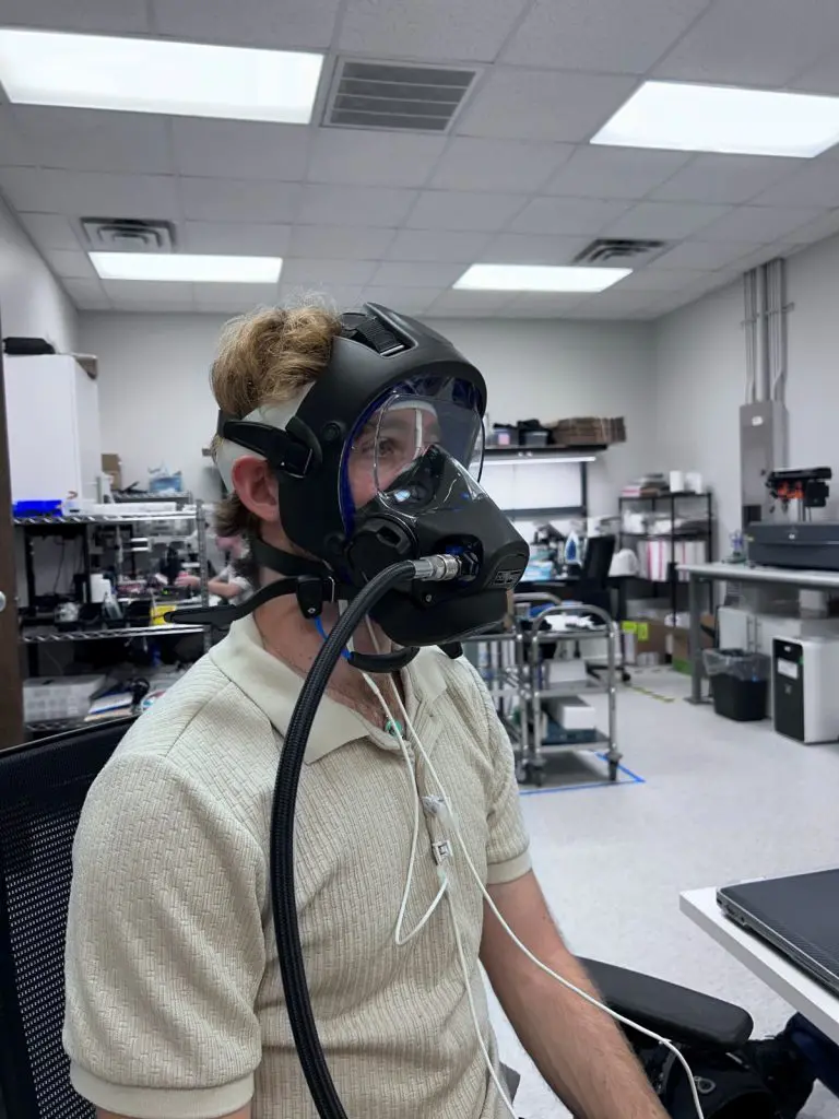 Trystan sits wearing a full face mask with a forehead and nasal alar pulse oximeter sensor underneath